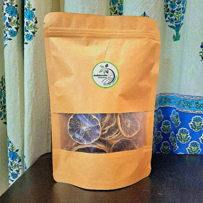 Brown paper bag with transparent window displaying dried lemon slices, against a patterned curtain background.